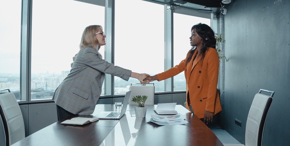 two women shaking hands over table