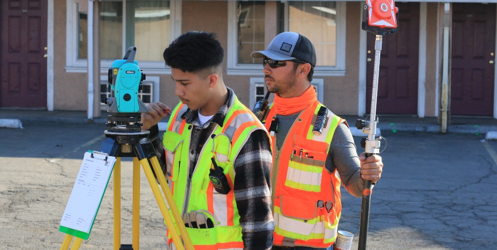 two men in high-vis jackets looking into tripod